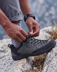 Close-up of DANNTO Veld I Gray barefoot shoes being tied on a rocky surface outdoors