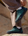 Person adjusting DANNTO Veld I green barefoot shoes while standing on rocks outdoors