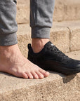 Dannto Aero N4 - 3E Wide Barefoot Shoes black shown on one foot beside a bare foot to demonstrate the wide toe box