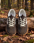 DANNTO Purus Men's and Women's Wide Toe Box Barefoot Shoes in Brown Shown Side by Side on a Forest Floor in Front of a Fallen Log.