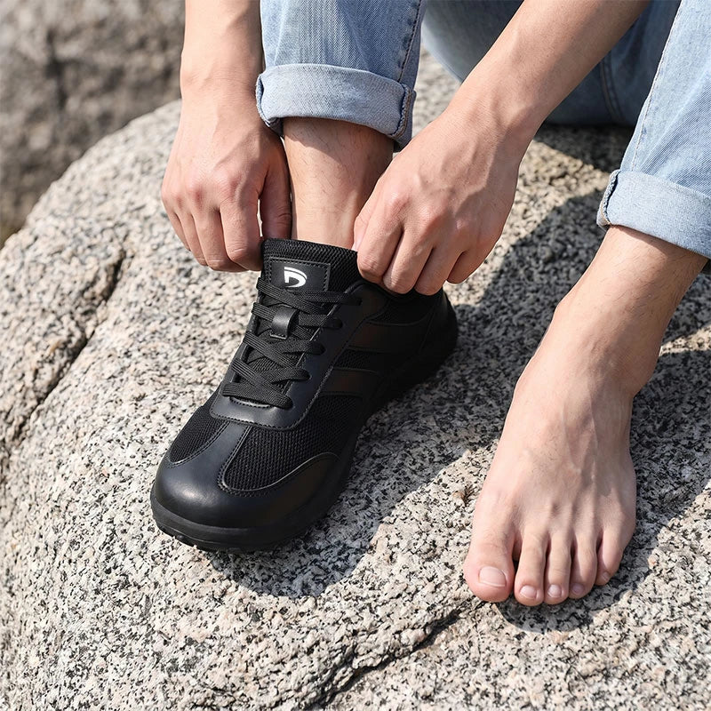 Dannto Frond - Non-Slip Zero Drop Barefoot Sneakers black shown being put on while sitting on a rock outdoors