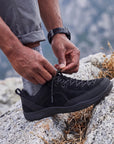 Close-up of DANNTO Veld I  Black barefoot shoes being tied on rocks outdoors