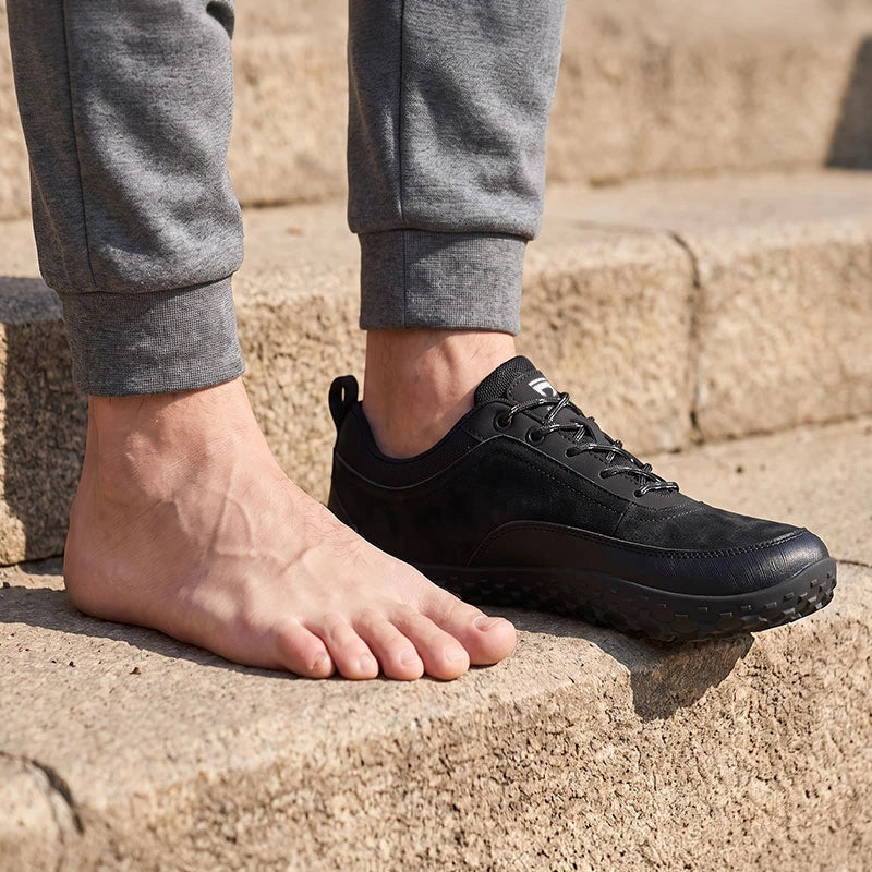 Dannto Aero N4 - 3E Wide Barefoot Shoes black shown on one foot beside a bare foot to demonstrate the wide toe box