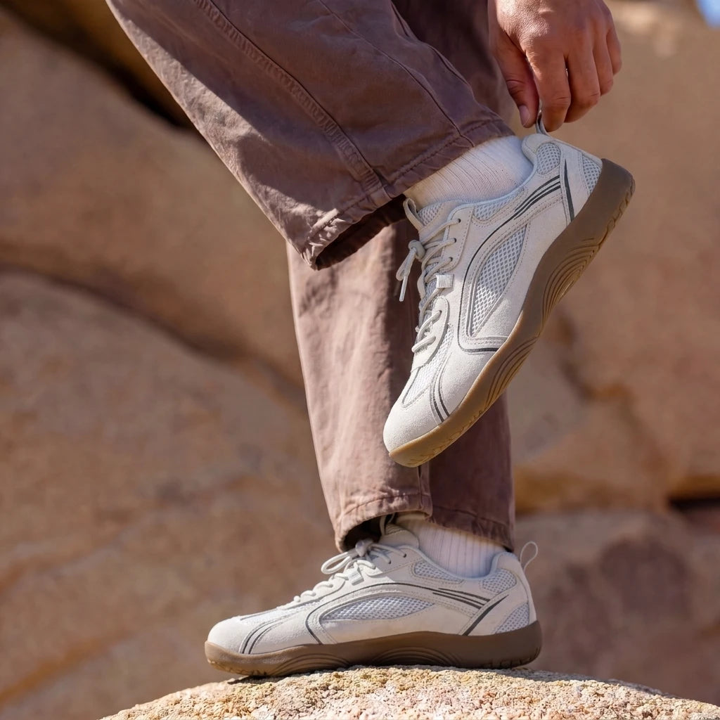 Person adjusting DANNTO Aero N1 white barefoot shoes while standing on rocks outdoors