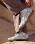 Person adjusting DANNTO Aero N1 white barefoot shoes while standing on rocks outdoors