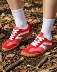 DANNTO Purus Men's and Women's Wide Toe Box Barefoot Shoes in Red Worn While Standing on a Leaf-Covered Forest Floor.
