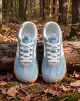 DANNTO Purus Men's and Women's Wide Toe Box Barefoot Shoes in Blue Shown Side by Side on a Forest Floor in Front of a Fallen Log.