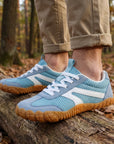 DANNTO Purus Men's and Women's Wide Toe Box Barefoot Shoes in Blue Worn While Walking Across a Fallen Log in a Forest.
