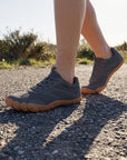 DANNTO Men's and Women's Wide Toe Box Barefoot Shoes in Gray Worn While Walking on a Sunlit Gravel Path.