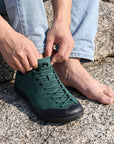 Dannto Veld I Pro - 3E Wide Barefoot Shoes green shown being put on while sitting on a rock outdoors