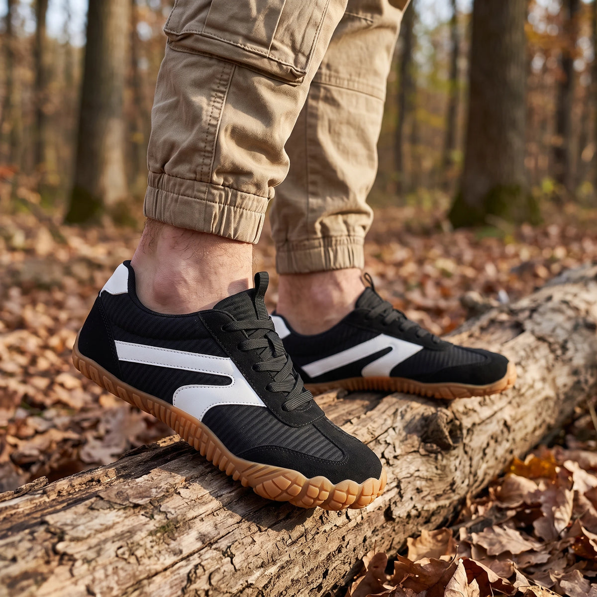 DANNTO Purus Men's and Women's Wide Toe Box Barefoot Shoes in Black Worn While Walking Across a Fallen Log in a Forest.