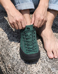 Dannto Veld I - Men's and Women's Wide Toe Box Barefoot Shoes green shown being put on while sitting on a rock outdoors