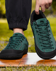 Dannto Veld I - Men's and Women's Wide Toe Box Barefoot Shoes green shown with one shoe worn and the other held by the heel outdoors