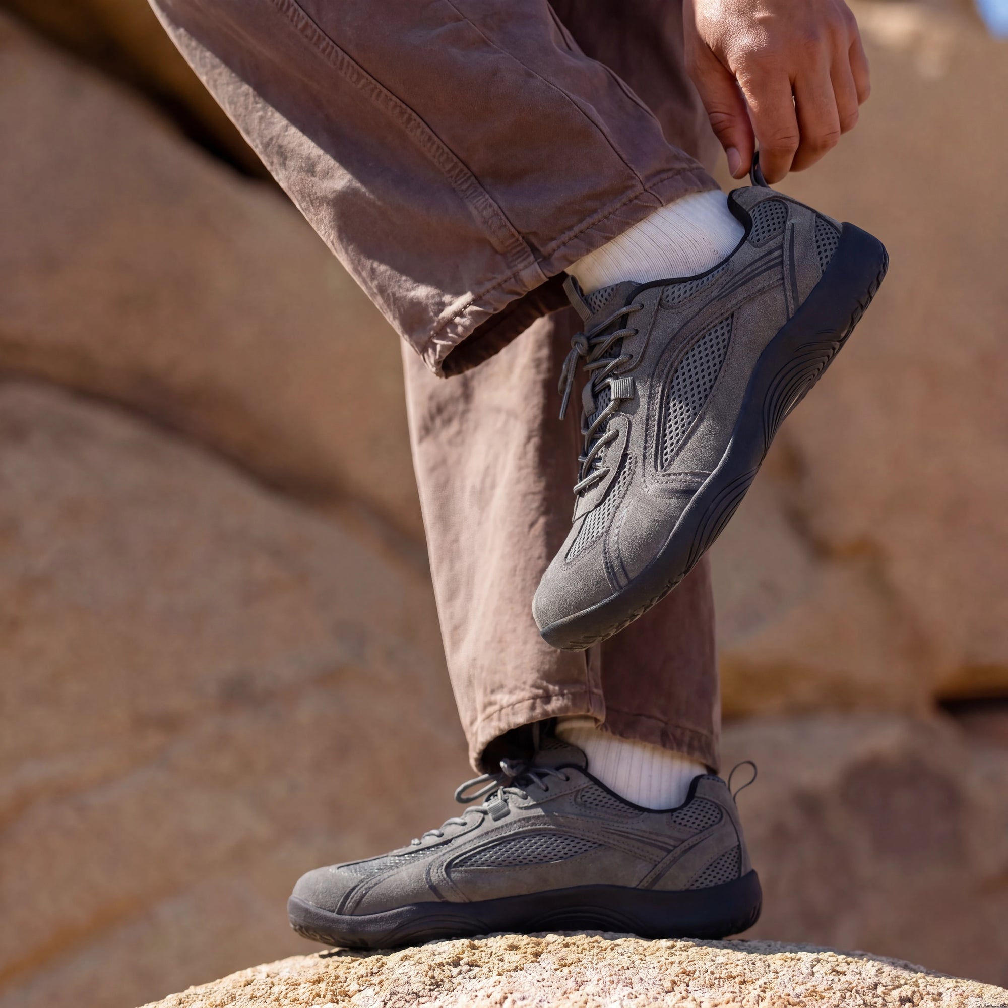Person adjusting DANNTO Aero N1 gray barefoot shoes while standing on rocks outdoors