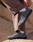 Person adjusting DANNTO Aero N1 gray barefoot shoes while standing on rocks outdoors