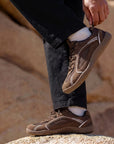 Person adjusting DANNTO Aero N1 brown barefoot shoes while standing on rocks outdoors